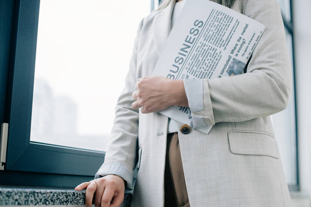cropped view of professional businesswoman holding business newspaper in office - Φωτογραφία, εικόνα