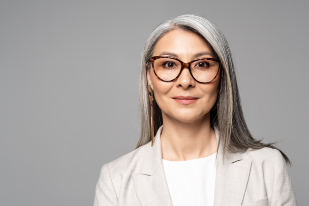 attractive smiling asian businesswoman in eyeglasses isolated on grey - Fotografie, Obrázek