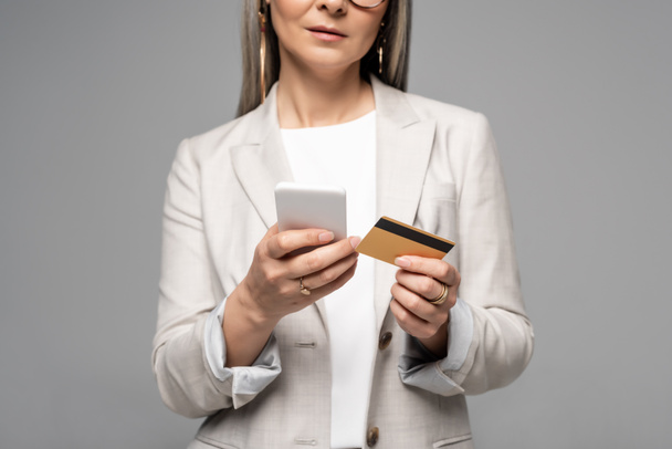 Gri saçlı, internetten alışveriş yapan, kredi kartı ve akıllı telefondan izole edilmiş iş kadını görüntüsü. - Fotoğraf, Görsel