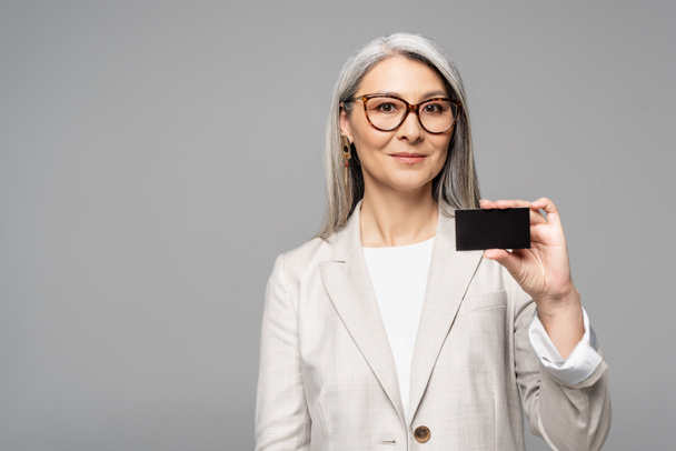 smiling asian businesswoman holding business card isolated on grey - Zdjęcie, obraz