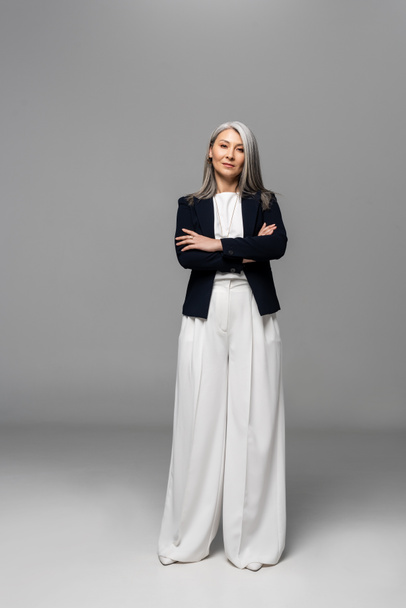 confident asian businesswoman with grey hair and crossed arms on grey - Foto, Bild