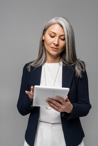 serious asian businesswoman using digital tablet isolated on grey  - Фото, зображення