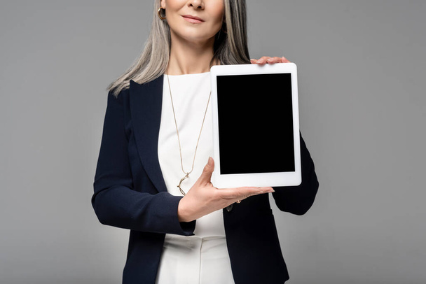 グレーで区切られた空白の画面を持つデジタルタブレットを提示ビジネス女性のクロップドビュー  - 写真・画像