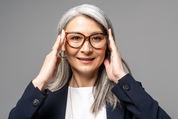 lächelnde asiatische Geschäftsfrau mit grauen Haaren in Brille isoliert auf grau - Foto, Bild