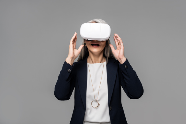 attractive surprised businesswoman using virtual reality headset isolated on grey - Foto, immagini