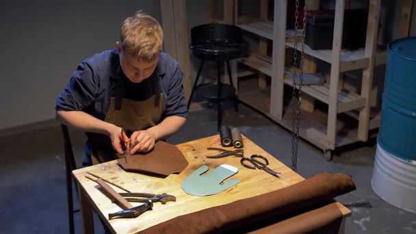 Чоловік вирізає шматок тканини для взуття на столі
  - Фото, зображення