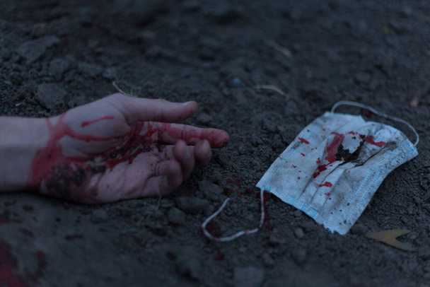 A medical bloodied mask lies on the ground with a bloody hand reaching out. The concept of coronavirus and the apocalypse resulting from this disease has spread throughout the world. Horror. - Valokuva, kuva