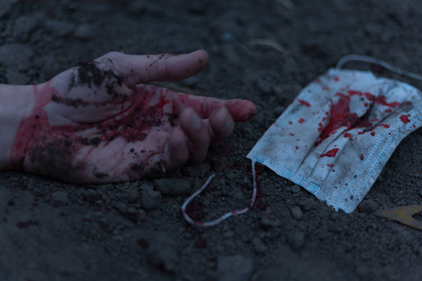 A medical bloodied mask lies on the ground with a bloody hand reaching out. The concept of coronavirus and the apocalypse resulting from this disease has spread throughout the world. Horror. - Photo, image