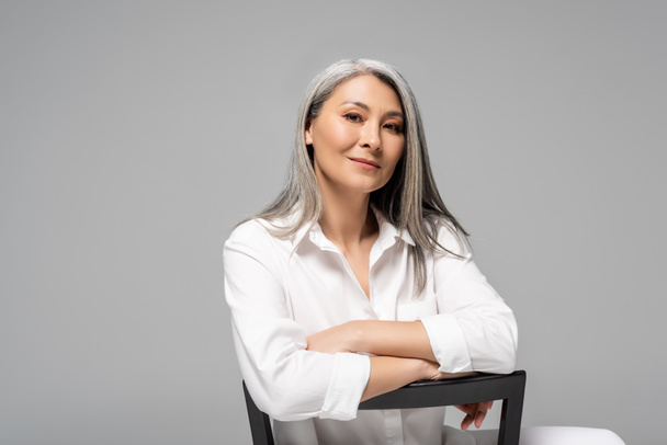attractive asian woman with grey hair sitting on chair isolated on grey - Foto, Imagem