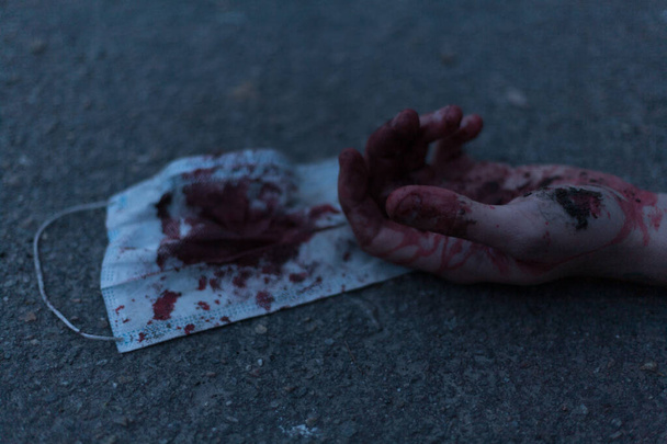 A medical bloodied mask lies on the ground with a bloody hand reaching out. The concept of coronavirus and the apocalypse resulting from this disease has spread throughout the world. Horror. - Photo, Image