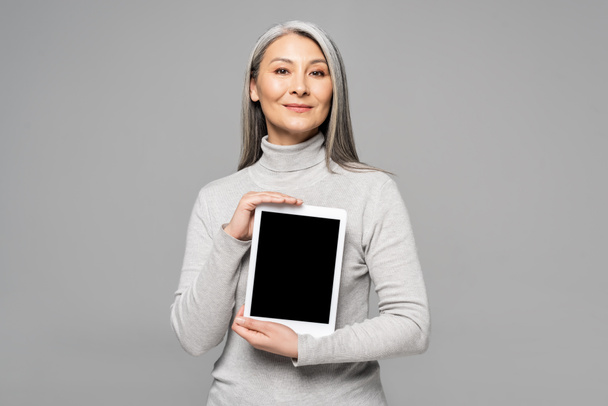 attractive asian woman presenting digital tablet with blank screen isolated on grey  - 写真・画像