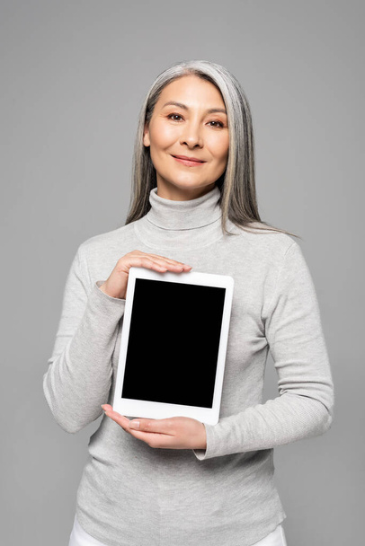 happy attractive asian woman presenting digital tablet with blank screen isolated on grey  - Photo, Image