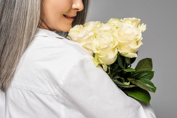 vista cortada de mulher adulta com cabelo grisalho segurando buquê de rosas brancas isoladas em cinza
 - Foto, Imagem