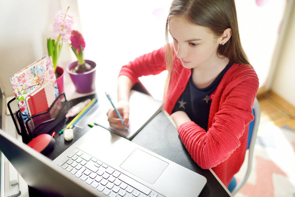 Liseli kız evde dizüstü bilgisayarla ödevini yapıyor. Çocuk çalışmak için aletler kullanıyor. Çevrimiçi eğitim ve çocuklar için uzaktan öğrenme. Karantina sırasında evde eğitim. Evde kal.. - Fotoğraf, Görsel