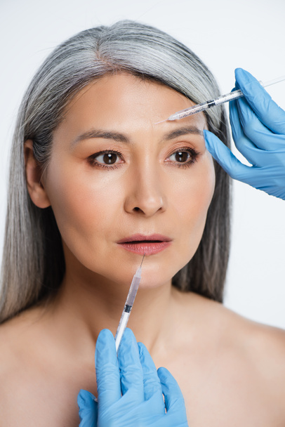 vonzó meztelen ázsiai nő és orvosok latex kesztyű gazdaság fecskendők szépség injekciók elszigetelt szürke - Fotó, kép