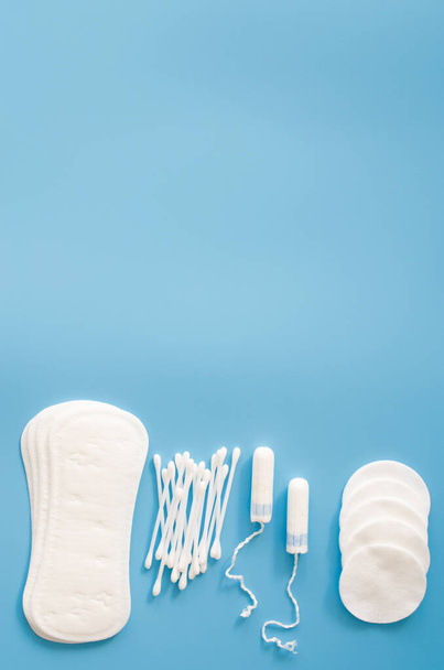 Weibliche Hygiene-Accessoires. Konzept der weiblichen Hygiene während der Menstruation. Damenbinden, Tampons, Wattestäbchen und Baumwollkissen auf blauem Hintergrund. Flache Lage, Draufsicht - Foto, Bild