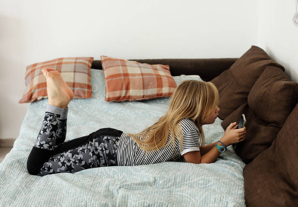 Covid-19. Heimschulkonzept. 9-jähriges Mädchen langweilt sich zu Hause mit Handy. - Foto, Bild