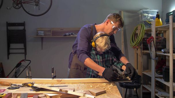 Maestro enseña a niño a pulir tablero de madera
 - Foto, Imagen