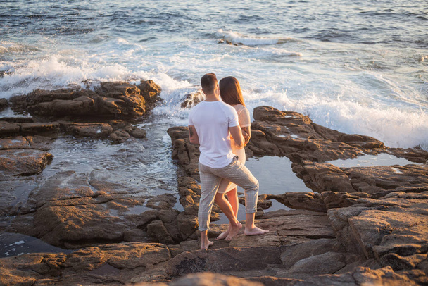 Joven pareja disfruta de su amor frente a una puesta de sol en el mar. - Foto, Imagen