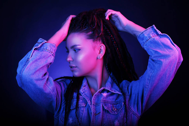 Sexy portrait of a young woman, in neon pink and blue light. Girl with dreadlocks in a nightclub, sexy turtleneck, radiant makeup with highlighter. Glitter skin. Clubber, night life concept - Foto, Imagem