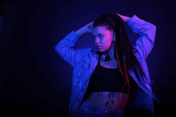 Sexy portrait of a young woman, in neon pink and blue light. Girl with dreadlocks in a nightclub, shining make-up with highlighter. Dance to music. Clubber, night life concept - Фото, изображение