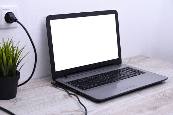 Laptop, a számítógép egy 220 voltos konnektorból tölt fel egy asztalt a fal mellett. Energia, felhalmozódás - Fotó, kép