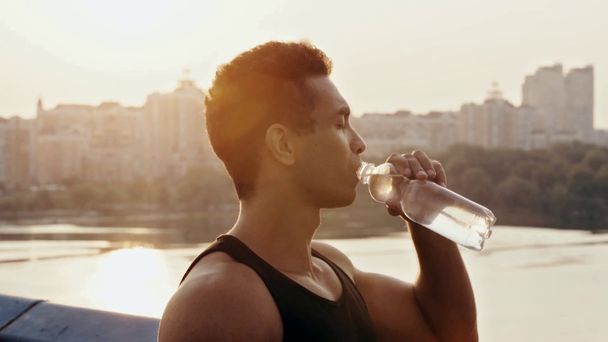 Sportler läuft, lächelt und trinkt Wasser auf Brücke - Filmmaterial, Video
