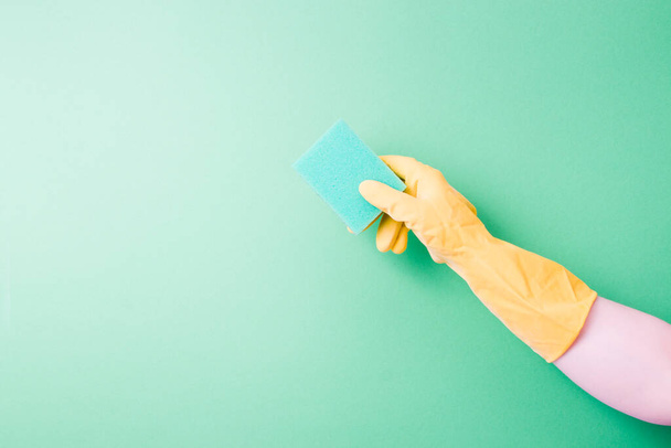 female hand in a rubber glove holds a green paralonne sponge for cleaning and washing dishes, green background copy space, company cleaning and spring cleaning concept - Φωτογραφία, εικόνα