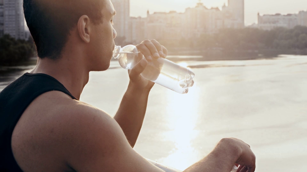 Sportler öffnet Flasche und trinkt Wasser auf Brücke - Filmmaterial, Video