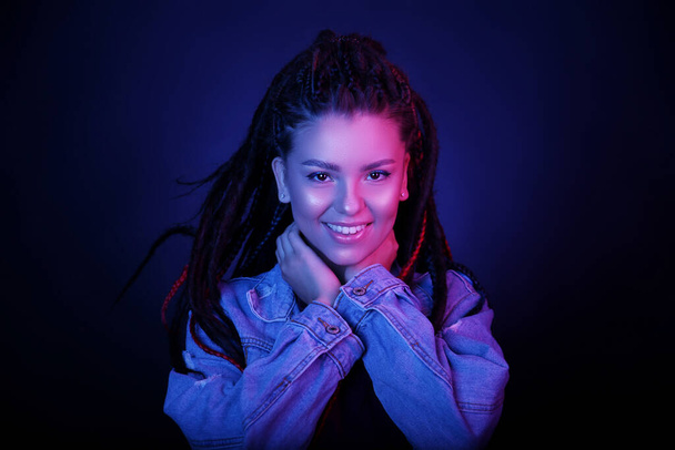 Sexy portrait of a young woman, in neon pink and blue light. Girl with dreadlocks in a nightclub, sexy turtleneck, radiant makeup with highlighter. Glitter skin. Clubber, night life concept - Valokuva, kuva