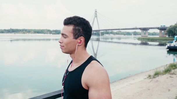 Esportista colocando fones de ouvido nos ouvidos e olhando para o rio
 - Filmagem, Vídeo