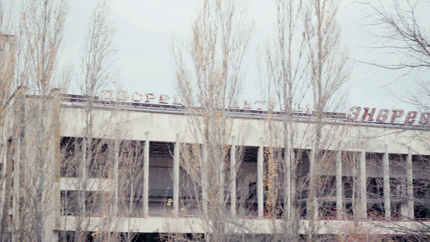CHERNOBYL UKRAINE - NOVEMBER 6, 2019: elhagyott épület kultúrpalotával és energetikai felirattal a fák közelében  - Felvétel, videó