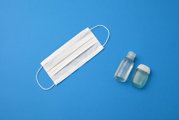 Einweg-Chirurgenmaske für den hygienischen Schutz und Händedesinfektionsmittel isoliert auf blauem Hintergrund. - Foto, Bild