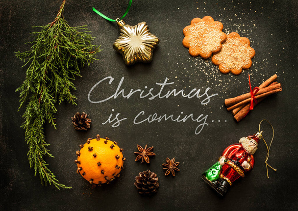 Christmas is coming - poster or postcard design. Vintage decorations, ginger cookies and spices on black chalkboard from above. - Фото, зображення