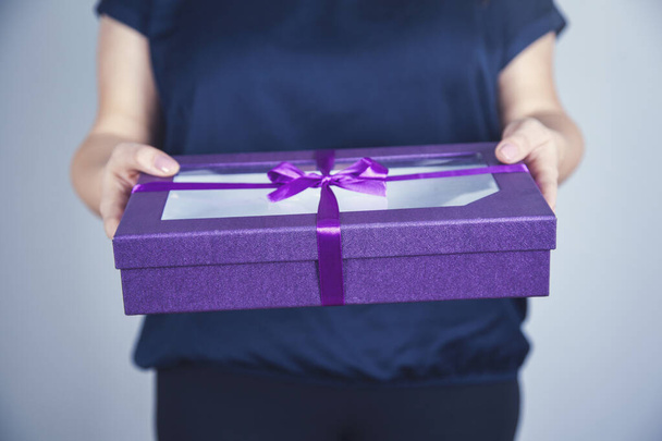 mujer mano celebración púrpura caja de regalo sobre fondo gris
 - Foto, imagen