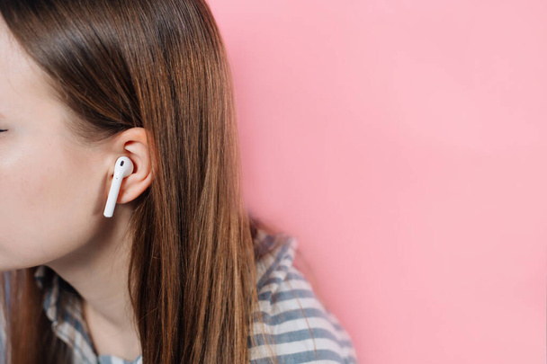 girl switches music on wireless headphones. Air Pods. with Wireless Charging Case. New Airpods 2019 on pink background. Airpods. female headphones. Copy Space - Foto, Imagem