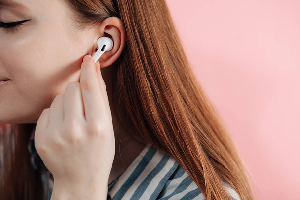 girl switches music on wireless headphones. Air Pods pro. with Wireless Charging Case. New Airpods  pro on pink background. Airpodspro. female headphones. Copy Space - Φωτογραφία, εικόνα