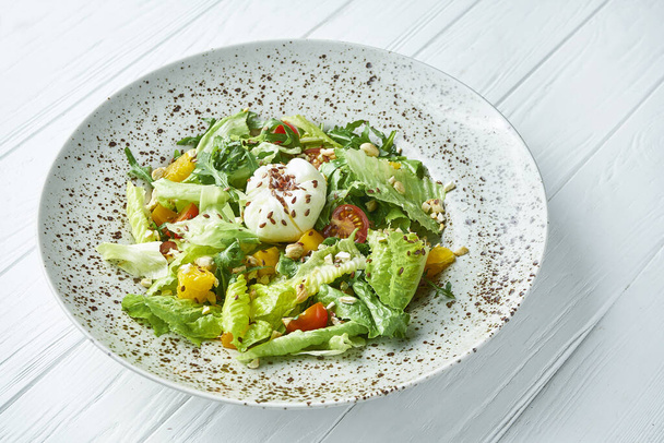 Close up view on Tasty juicy, green salad with lettuce, cherry tomatoes, pineapples and burrata cheese in a ceramic plate on a white wooden background - Photo, image