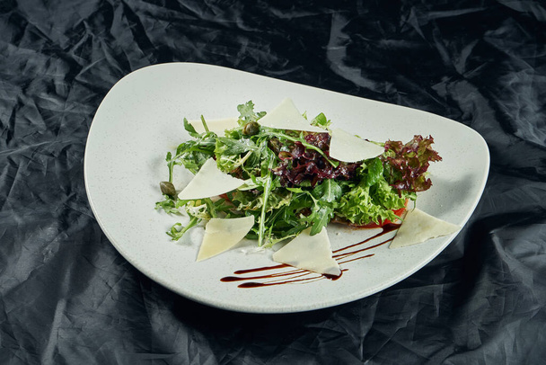 Close up view on Warm salad with parmesan, arugula, lettuce seasoned with truffle salsa on a white plate on a wooden background. Healthy food for diet. Vegetarian food - Photo, Image