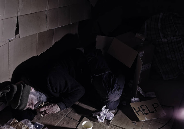 Бездомний бородатий чоловік сидить на коробках на вулиці і просить про допомогу. Потрібна безпритульна людина просить гроші на їжу і на ніч
. - Фото, зображення