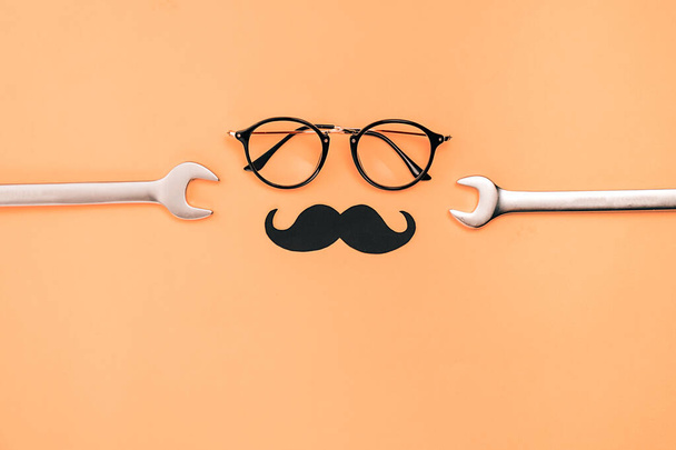 Fathers Day mockup with eyeglasses, combination wrenches and retro stylish black paper photo booth props moustaches on orange background with copy space. Flat lay, top view, minimal composition - Фото, изображение