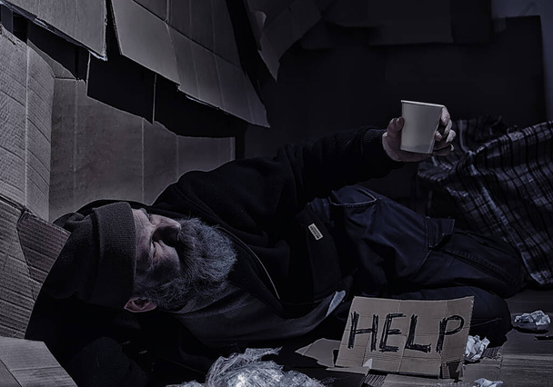 Evsiz sakallı bir adam sokakta kutulara oturup yardım istiyor. Evsiz bir insan yemek için para ister ve bir gecede. - Fotoğraf, Görsel
