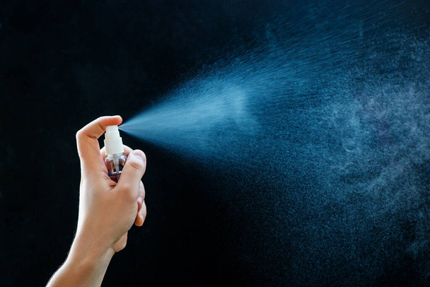Close up of using antibacterial hand spray on black background. - Foto, afbeelding