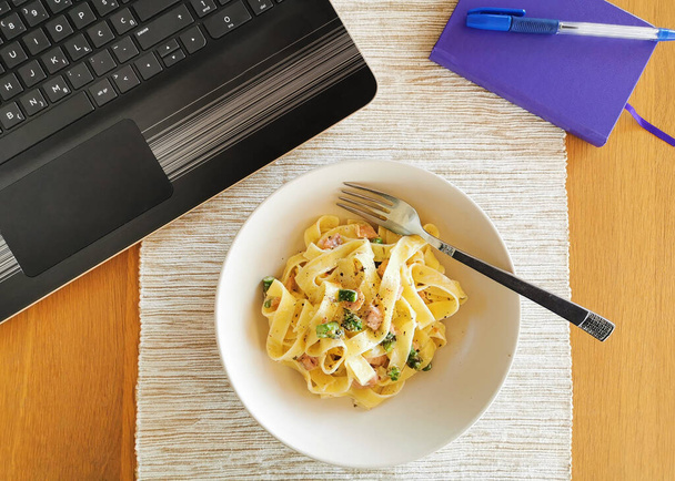 Обед во время работы из дома, миска макарон с лосося и спаржи и ноутбука и компьютерной мыши на стороне
 - Фото, изображение