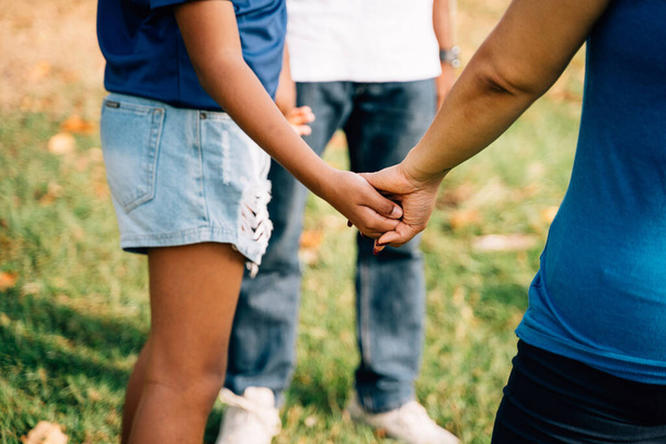 Hopeful family of father and teenage daughter, and mother holding hands together in circle and praying in outdoor park. Prayer of Catholic Jesus Christ and Thanksgiving concept. Close-up on hand - Foto, Imagen