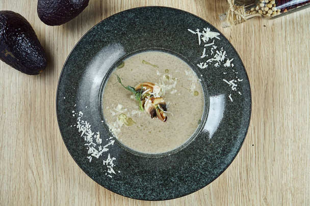 Mushroom cream soup with champignons, garnished with fried mushrooms, olive oil and grated Parmesan cheese in grey bowl on a wooden background. Healthy diet. Top view food - Valokuva, kuva