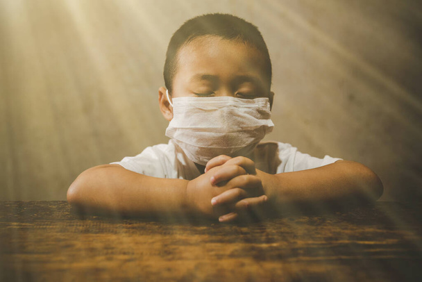 Μικρό αγόρι που φοράει μάσκα για προστασία PM2.5 και Covid-19. Προσεύχεται το πρωί για μια νέα μέρα ελευθερίας για τον ιό Γουχάν Κορόνα. Ασιάτης προσεύχεται, δόξα τω Θεώ. Αντιγραφή χώρου. - Φωτογραφία, εικόνα