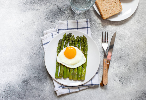 Gesunder Bio-Spargel und Spiegelei auf einem weißen Teller. Gesundes vegetarisches Frühstück. Grauer Hintergrund. Kopierraum. Flache Lage - Foto, Bild