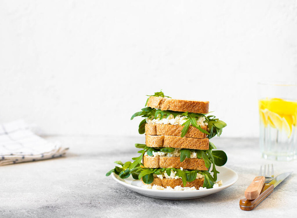 Egészséges szendvics ricottával és arugulával, világos szürke asztalon és fehér háttérrel. Egészséges reggeli. Közelkép. Fénymásolási hely - Fotó, kép