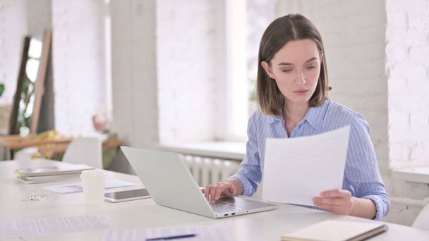 Зосереджена молода жінка читає документи і працює на ноутбуці
 - Фото, зображення